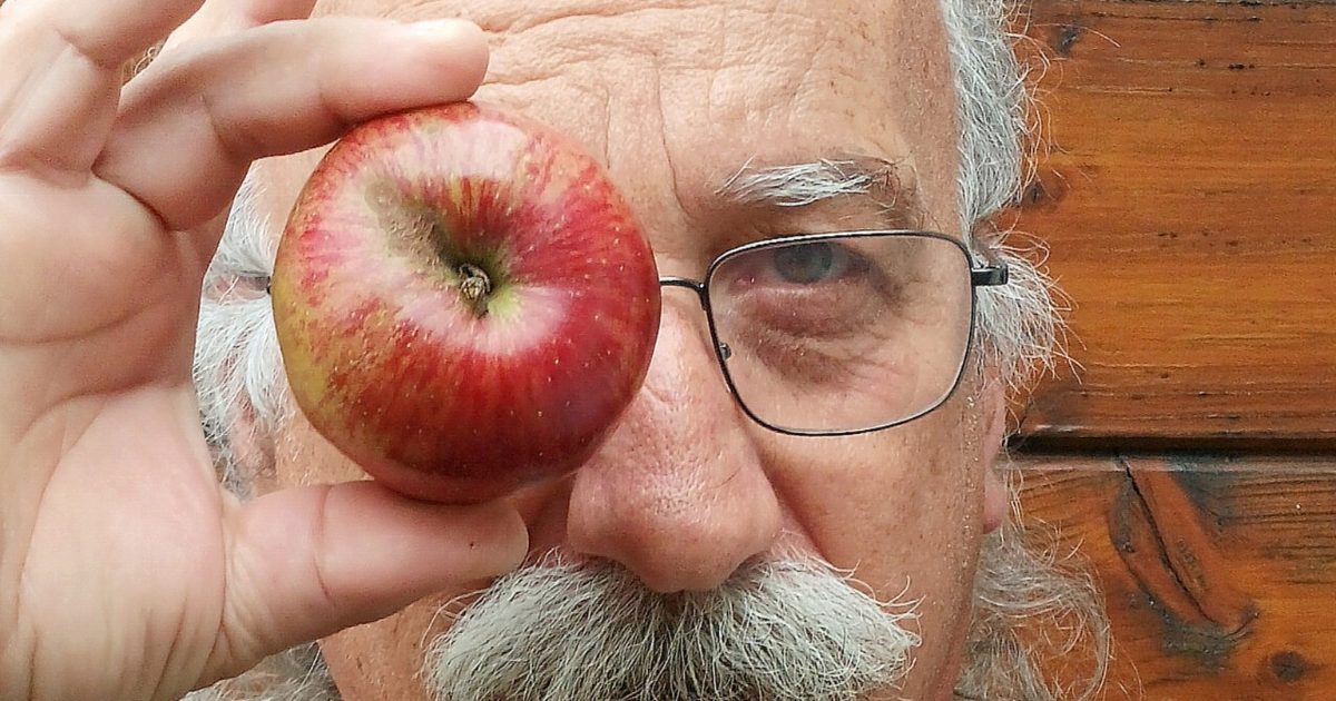 Gros plan d'un homme avec une moustache tenant une pomme devant son œil.